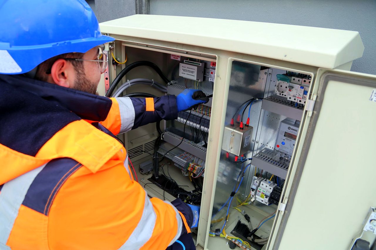 Elektriker arbeitet an einem Schaltschrank mit Sicherungen und Verdrahtung.
